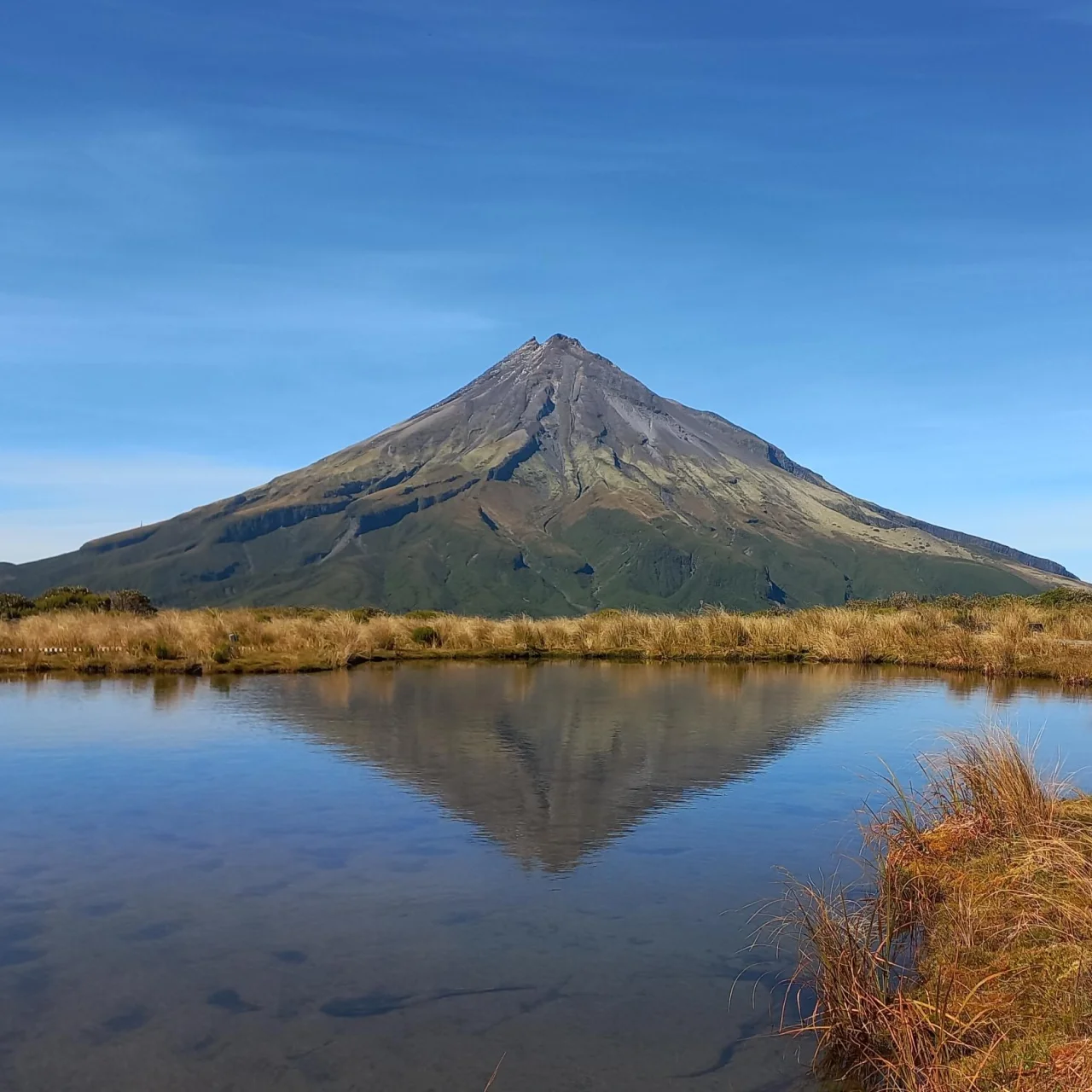 Mount Taranaki in de zon met de weerspiegeling in de tarns