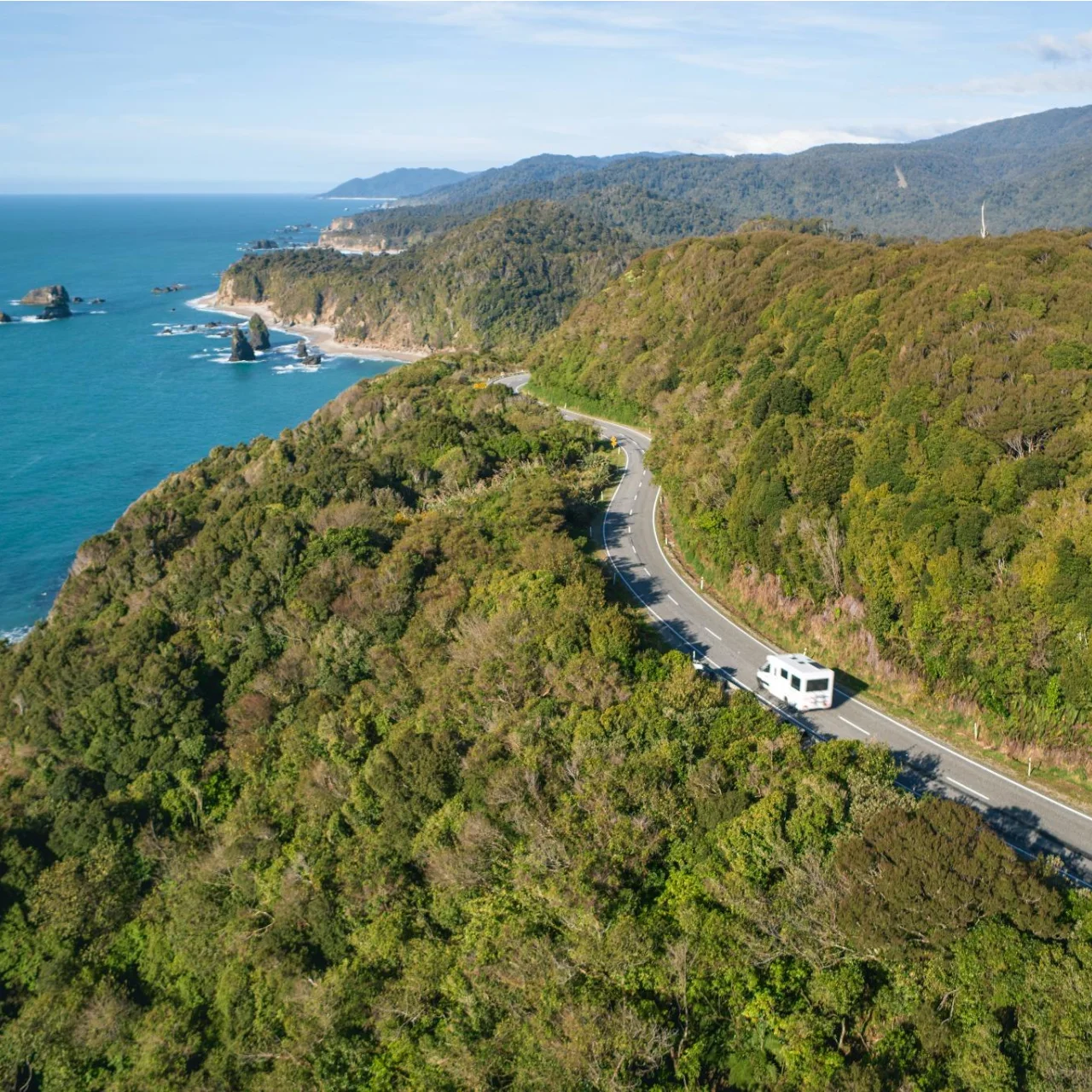 Camper op de weg langs de westcoast omringd door bossen en prachtig kronkelende kustlijnen, Haast Pass, Nieuw-Zeeland