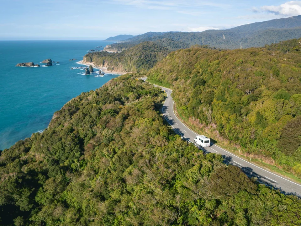 Camper op de weg langs de westcoast omringd door bossen en prachtig kronkelende kustlijnen, Haast Pass, Nieuw-Zeeland