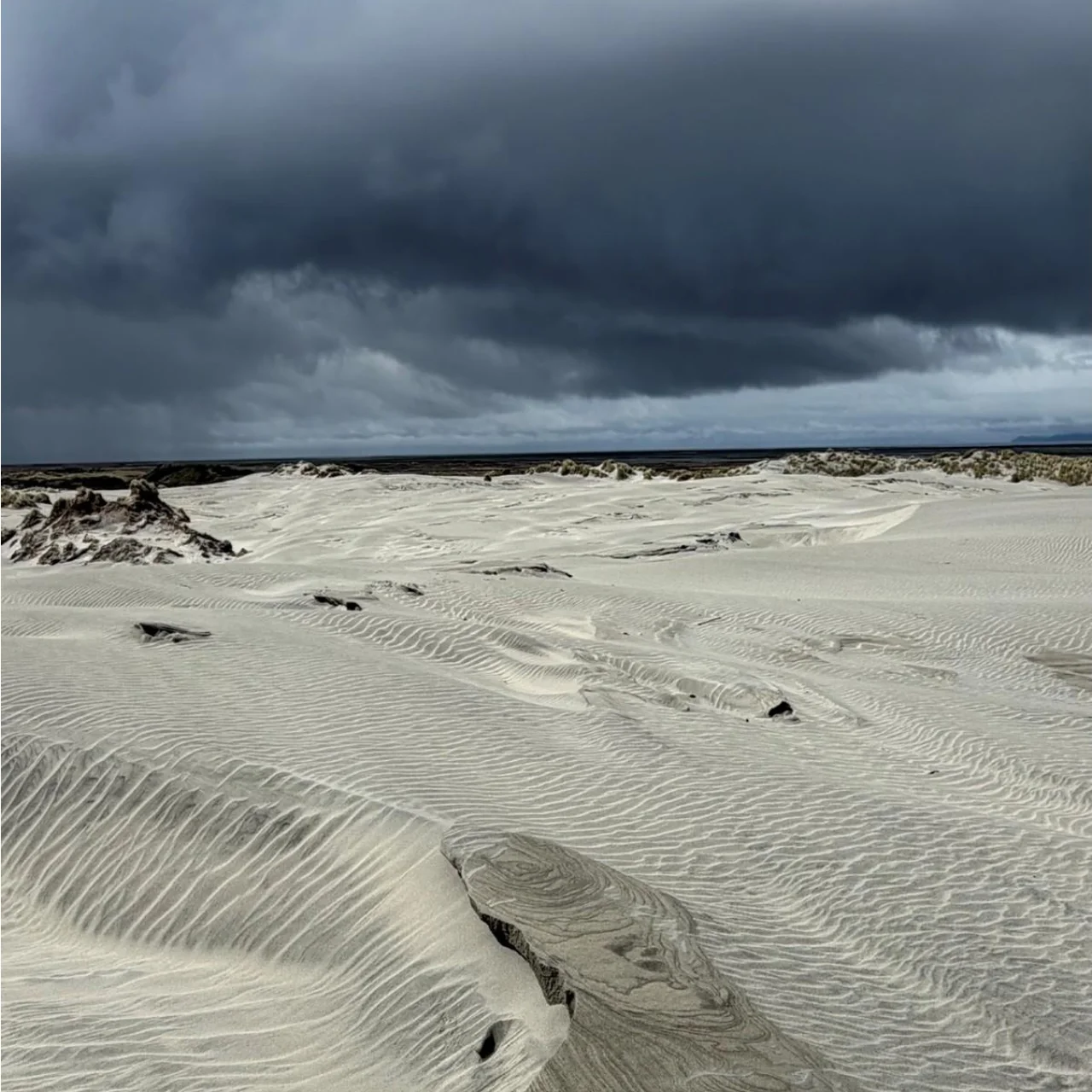 Zandduinen op het verlate strand in de Golden Bay, terwijl de onweerslucht nadert