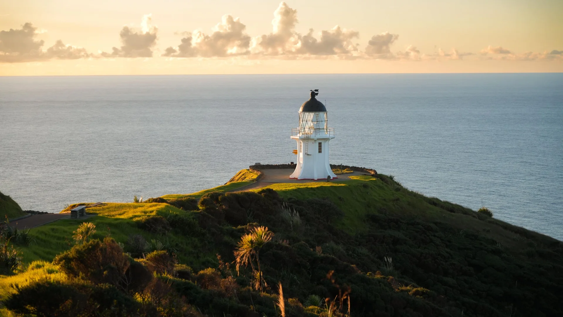 De vuurtoren bij Cape Reinga met de oceaan en ondergaande zon op de achtergrond, Nieuw-Zeeland