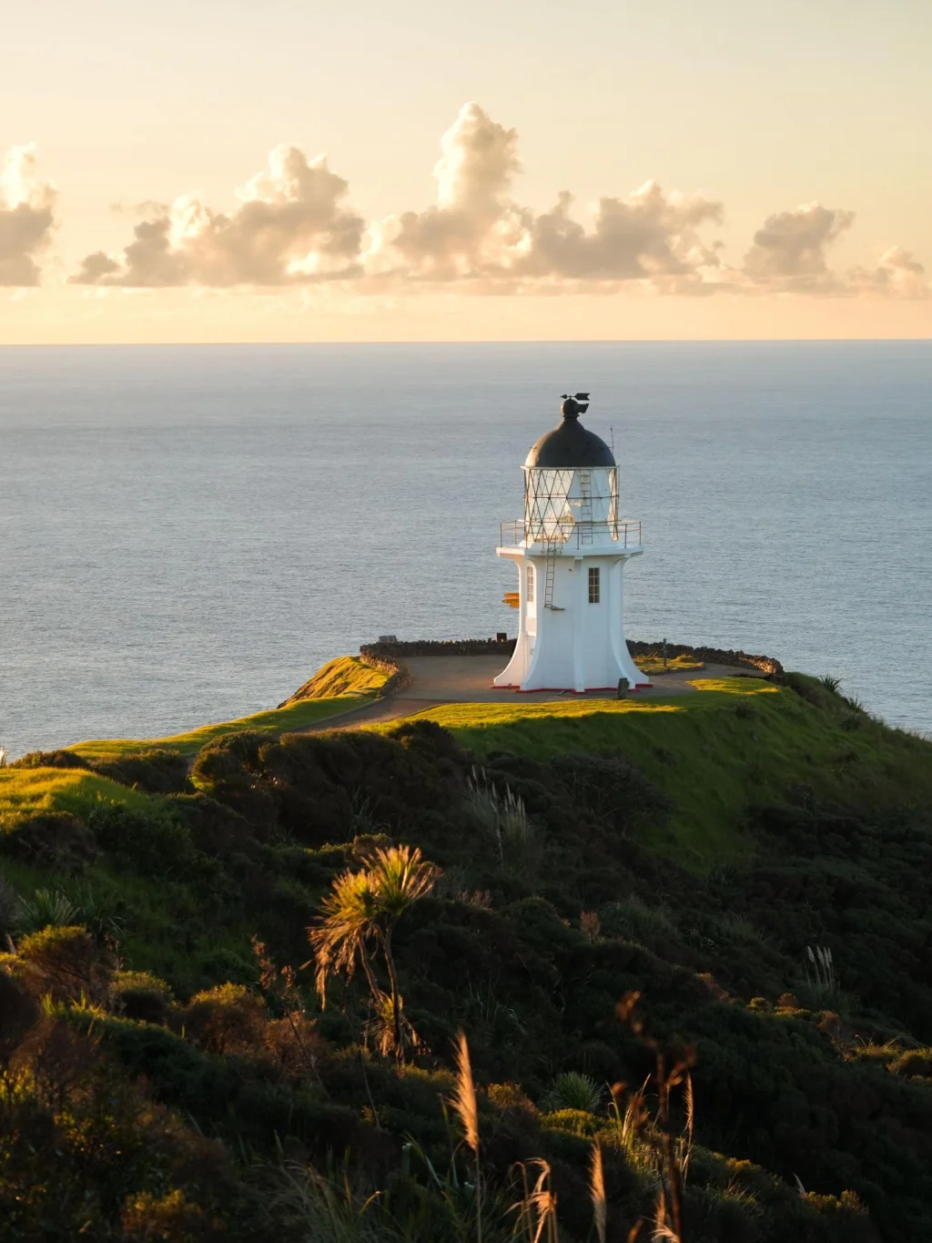 De vuurtoren bij Cape Reinga met de oceaan en ondergaande zon op de achtergrond, Nieuw-Zeeland