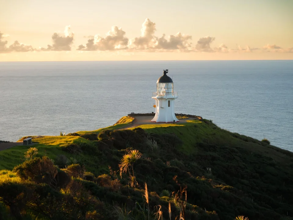 De vuurtoren bij Cape Reinga met de oceaan en ondergaande zon op de achtergrond, Nieuw-Zeeland
