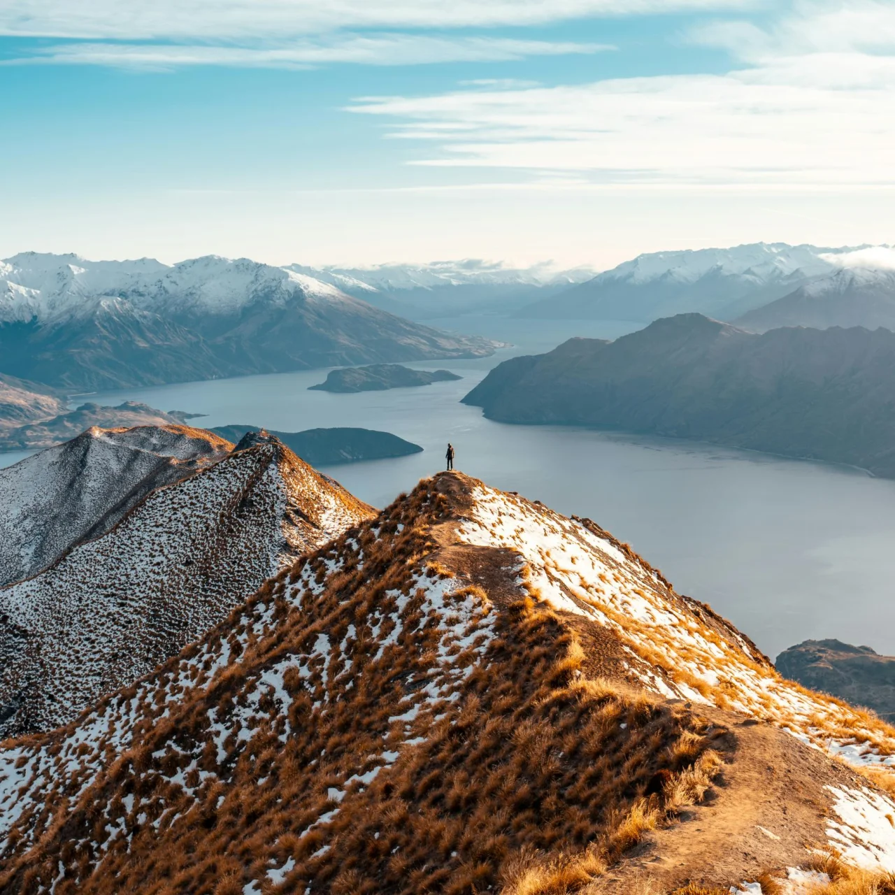 Wandelaar bovenop Roys Peak met uitzicht over de meren en besneeuwde bergtoppen, in Wanaka, Zuidereiland Nieuw-Zeeland
