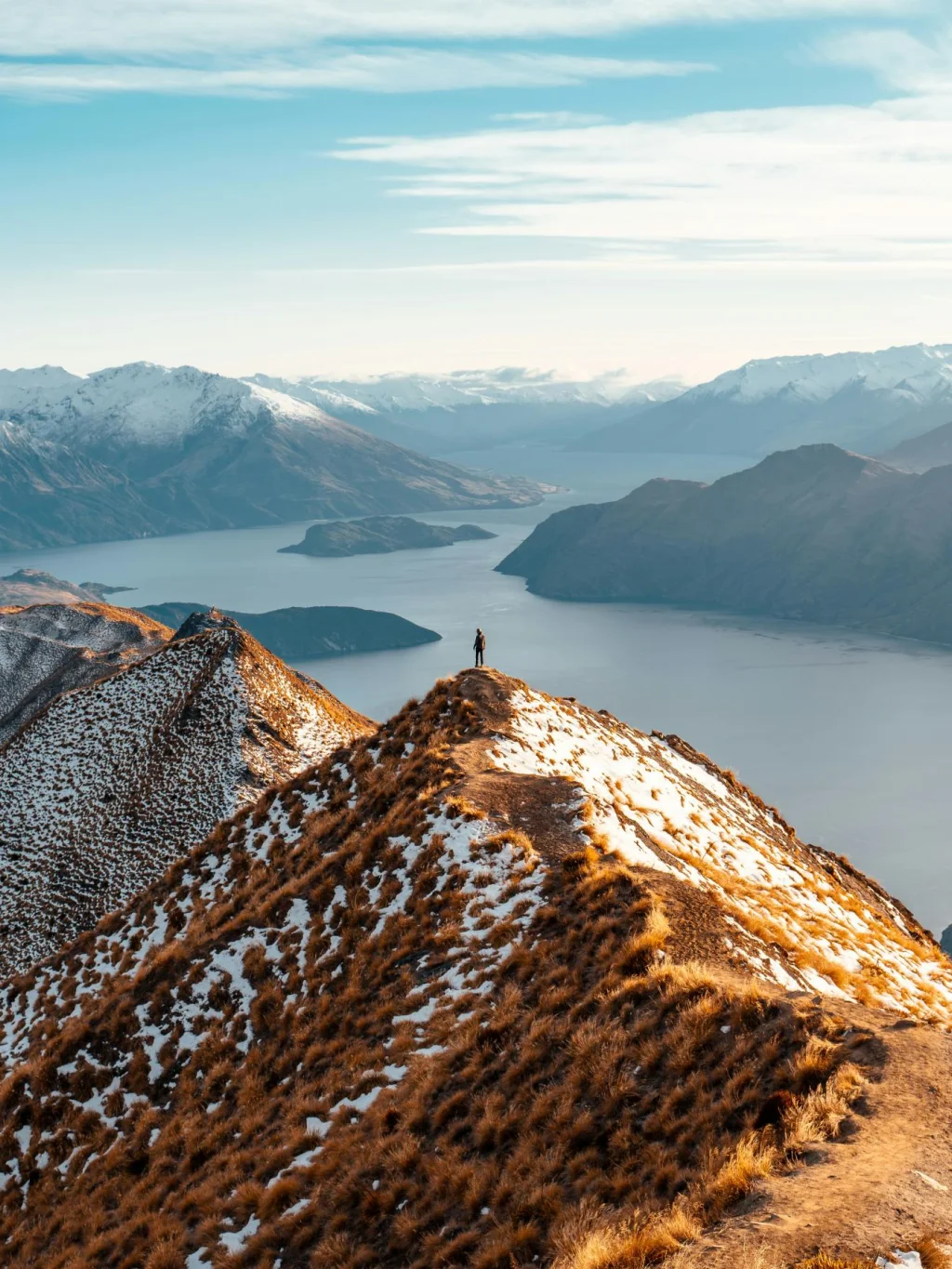 Wandelaar bovenop Roys Peak met uitzicht over de meren en besneeuwde bergtoppen, in Wanaka, Zuidereiland Nieuw-Zeeland
