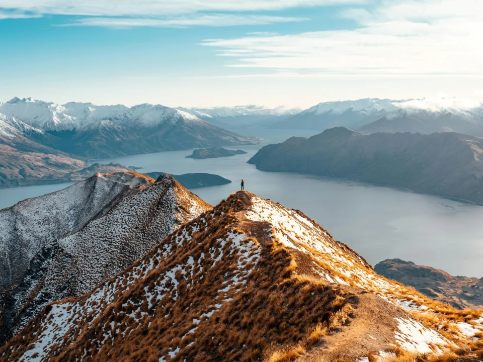 Wandelaar bovenop Roys Peak met uitzicht over de meren en besneeuwde bergtoppen, in Wanaka, Zuidereiland Nieuw-Zeeland