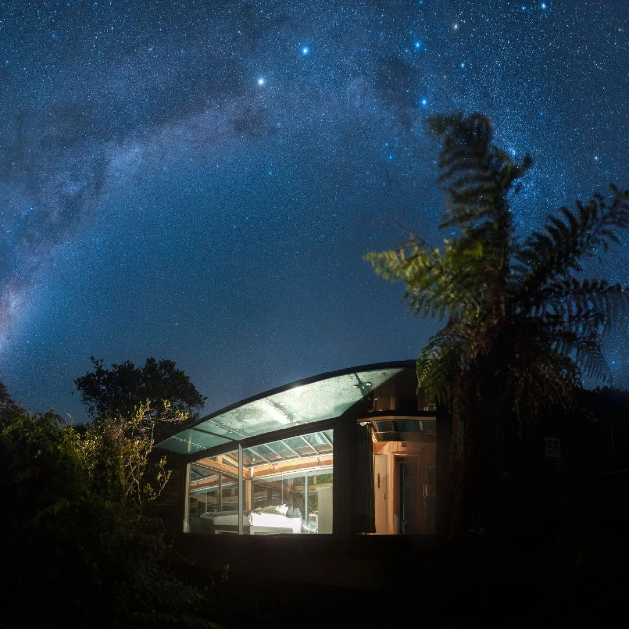 Glazen huisje Tokoeka PurePod in de nacht onder een prachtige sterrenhemel, op Stewart Island in Nieuw-Zeeland