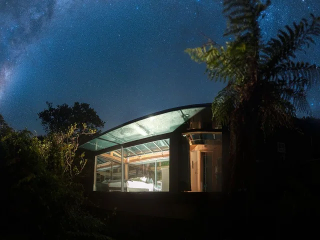 Glazen huisje Tokoeka PurePod in de nacht onder een prachtige sterrenhemel, op Stewart Island in Nieuw-Zeeland
