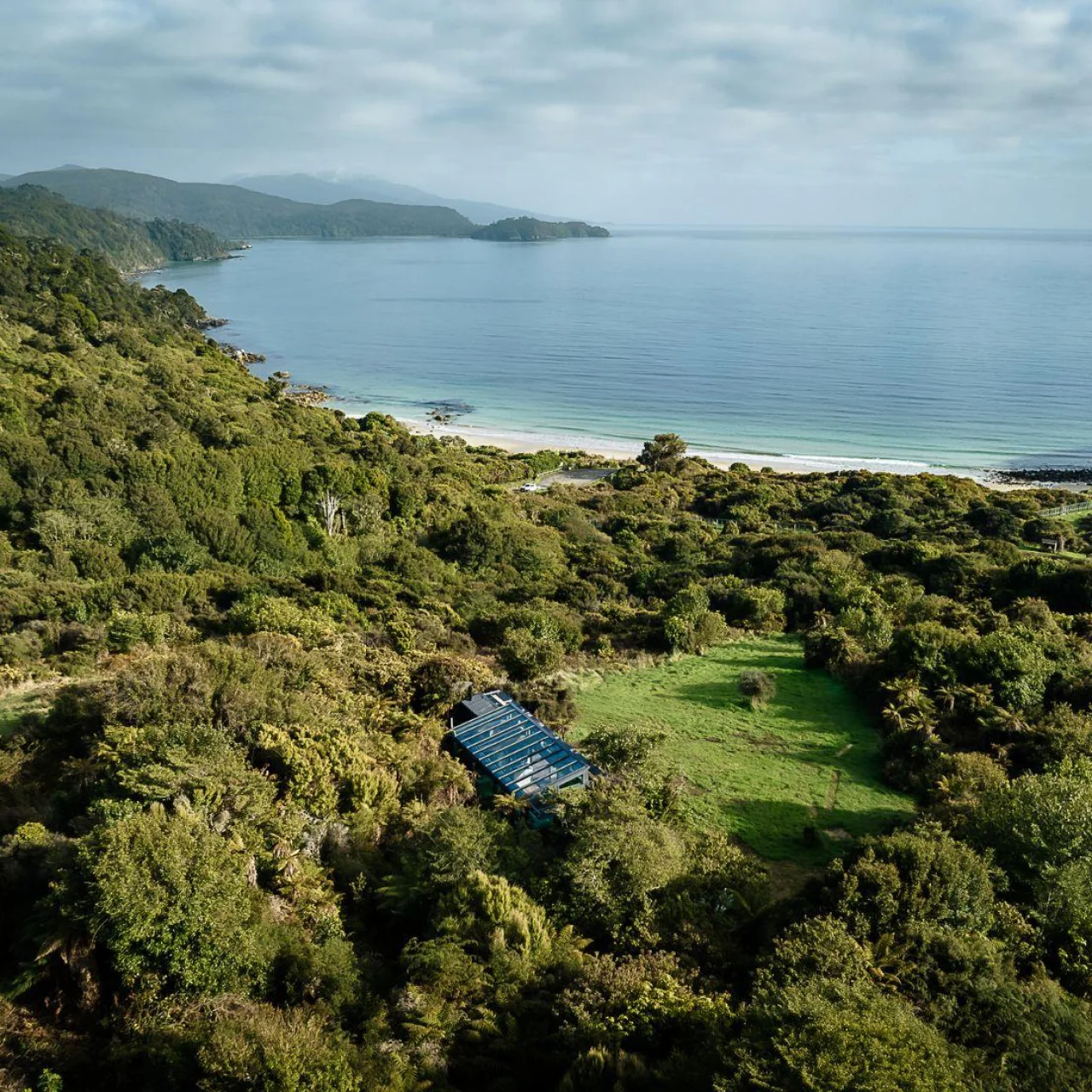 Glazen huisje Tokoeka PurePod ligt middenin het groen en kijkt uit over een prachtige baai, op Stewart Island in Nieuw-Zeeland