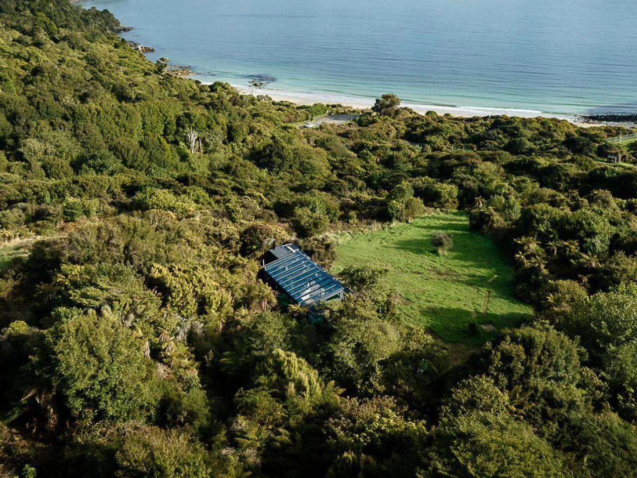 Glazen huisje Tokoeka PurePod ligt middenin het groen en kijkt uit over een prachtige baai, op Stewart Island in Nieuw-Zeeland