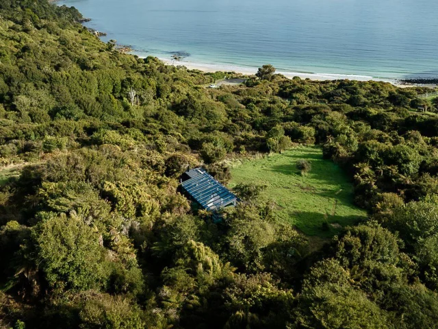 Glazen huisje Tokoeka PurePod ligt middenin het groen en kijkt uit over een prachtige baai, op Stewart Island in Nieuw-Zeeland